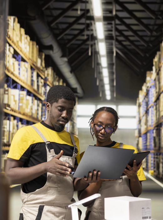 Black employees checking inventory and shipment details on laptop before applying awb tags. Large scale distribution operations with structured workflow and efficient merchandise tracking.